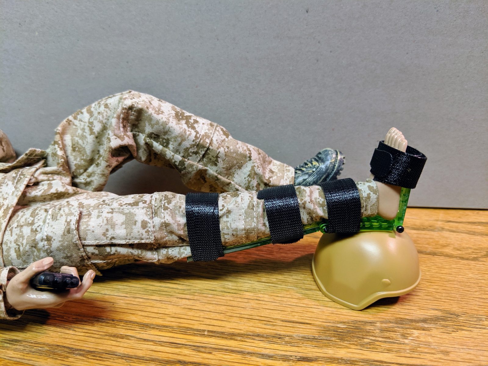 Neon-green Set-Lock Splint prototype locking an action-figure ankle at 90 degrees on a clean wood bench